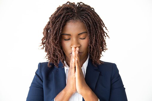 Hopeful young businesswoman praying. portrait of young African American businesswoman standing with closed eyes and praying isolated on white background. Business and belief concept